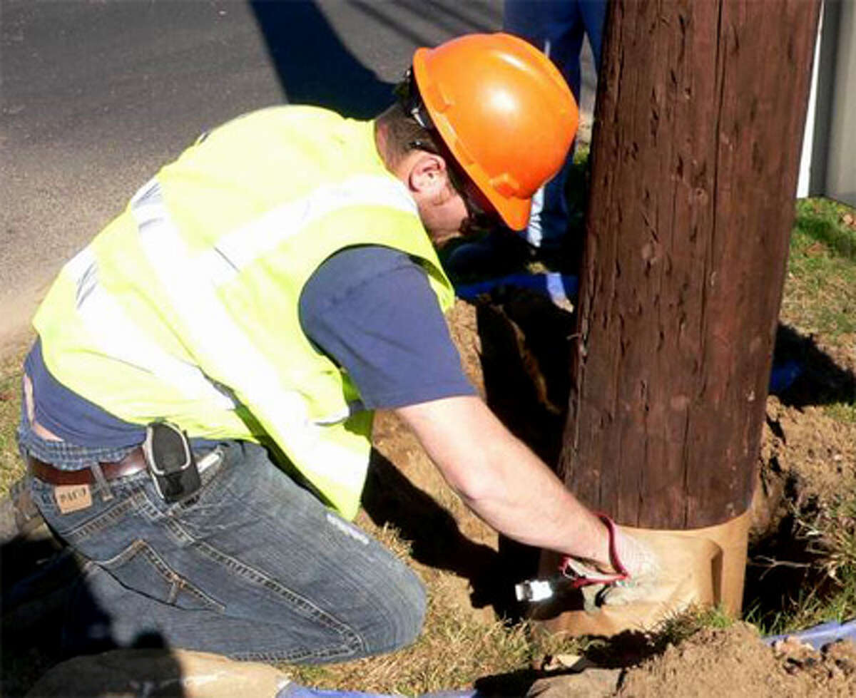 A worker wraps a United Illuminating pole's base after treating it with a chemical agent to prevent decay.