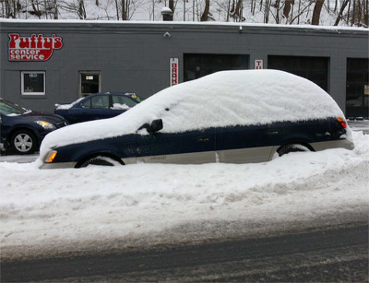 A snow-covered vehicle on the side of the road in downtown Shelton.