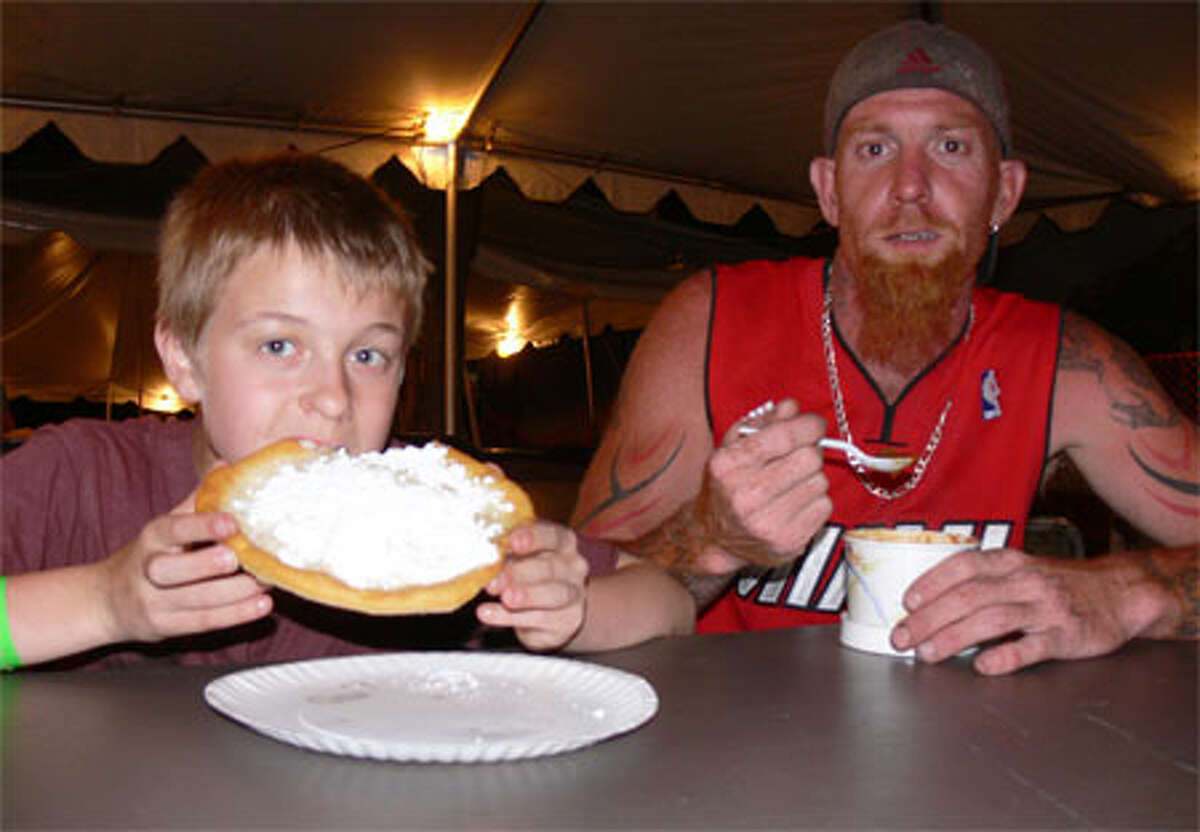 Fred Davino, 10, of Shelton bites into his fried dough with powdered sugar during the 2013 St. Joseph Carnival while joined by his father, Carl, who is enjoying a bowl of chili.