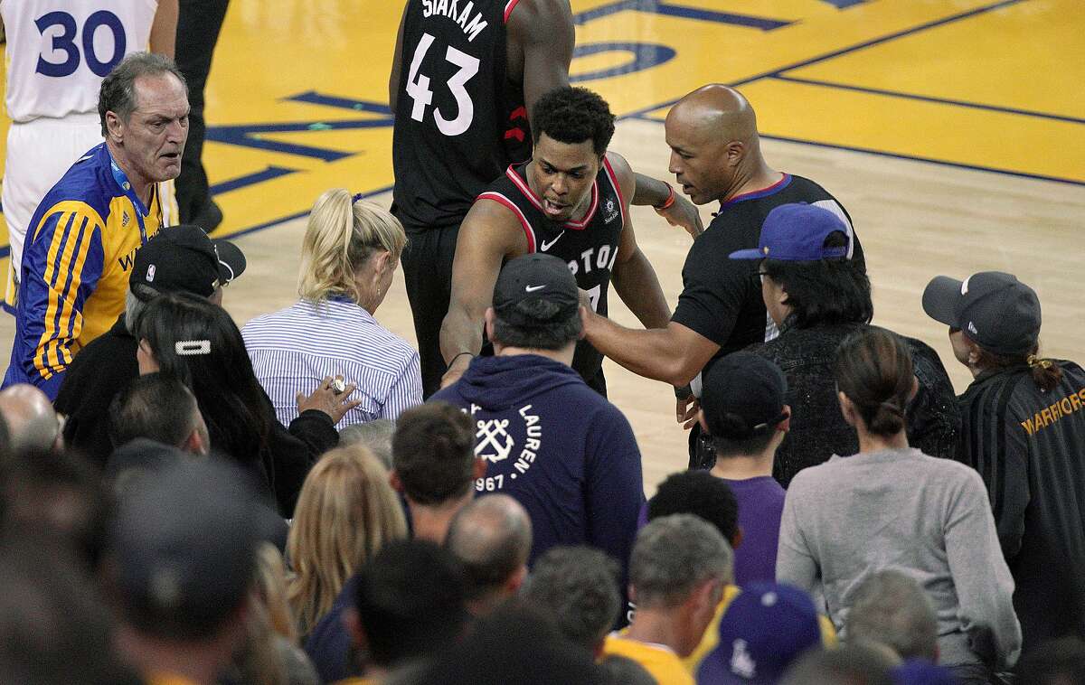 Toronto Raptors guard Kyle Lowry, middle, gestures next to referee Marc Davis (8) near the front row of fans during the second half of Game 3 of basketball's NBA Finals between the Golden State Warriors and the Raptors in Oakland, Calif., Wednesday, June 5, 2019. A fan seated courtside for Game 3 of the NBA Finals was ejected after shoving Lowry when the Raptors star crashed into a row of seats while trying to save a ball from going out of bounds on Wednesday night. (AP Photo/Tony Avelar)