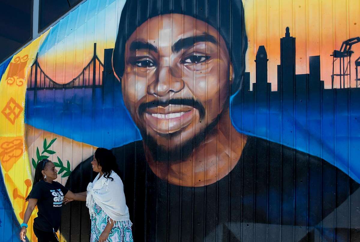 Wanda Johnson (right), mother of the late Oscar Grant, greets a friend while standing underneath a large mural honoring her son during a mural and street naming unveiling for Oscar Grant at Fruitvale BART Station in Oakland, Calif. Saturday, June 8, 2019.