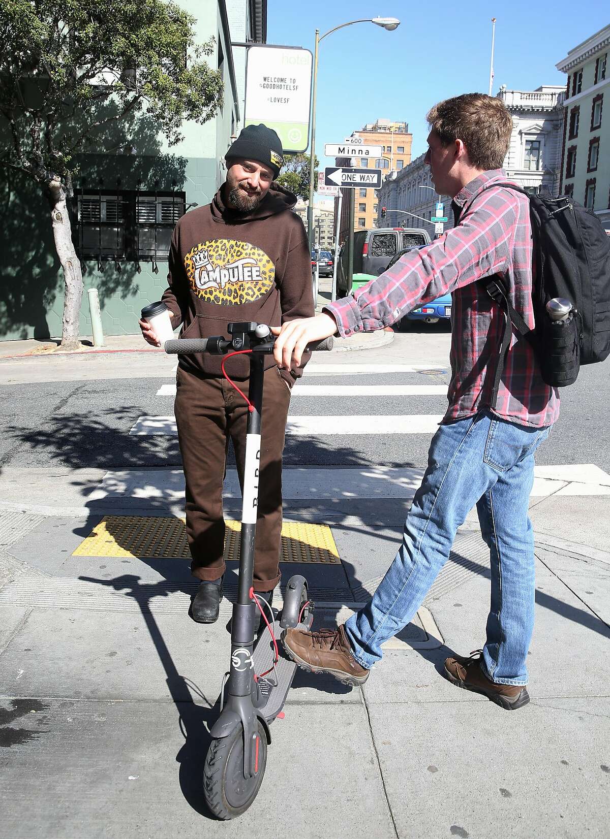 Adam Mesnick (left) who has sandwich shops in his neighborhood talks with Drew Lazzeri (right) riding a scooter on 7th Street on Friday, April 20, 2018, in San Francisco, Calif.