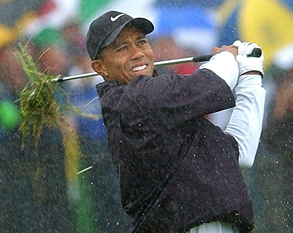 In this July 20, 2002 file photo, Tiger Woods plays from the rough, in the rain, on the first hole during the third round of the British Open Golf Championship at Muirfield golf course in Scotland. (AP Photo/Adam Butler)