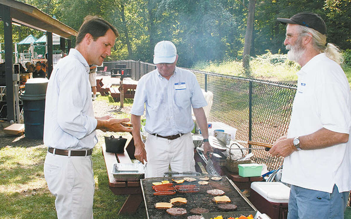 Congressman Jim Himes, left, gets a burger at last year’s barbecue. Manning the grill are Richard Creeth, center, and Paul Burnham.