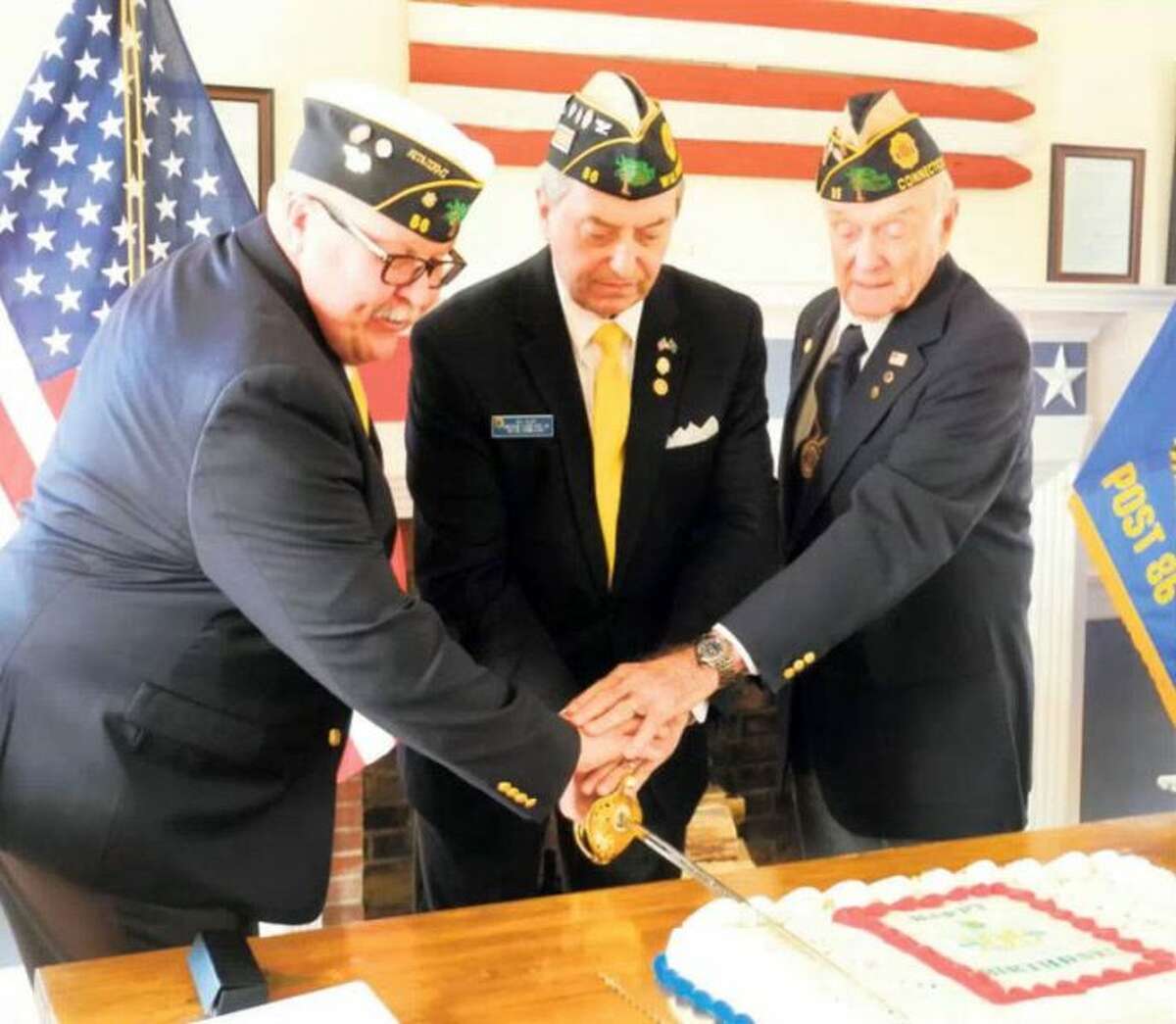 From left, Tom Moore, Bill Glass and Bing Ventres use a ceremonial sword to cut a cake celebrating the 100th anniversary of the American Legion at Post 86. — Jeannette Ross/Hearst Connecticut Media