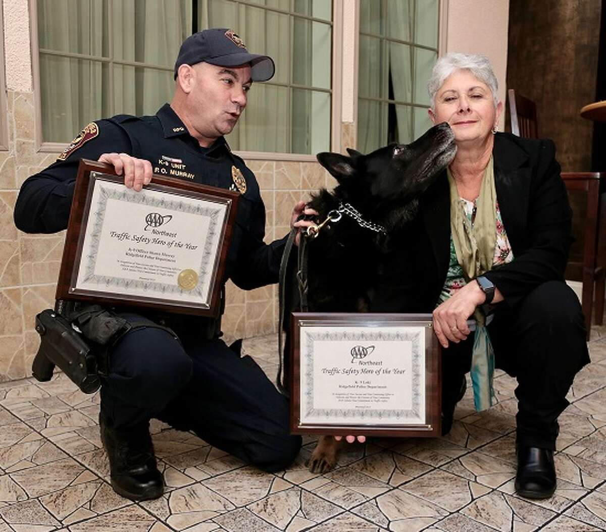 Ridgefield Police Department K9 officer Loki, a German Shepherd, gives AAA Northeast's Fran Mayko, right, a thank you kiss for his AAA Traffic Safety Hero award as his very surprised partner, K9 Officer Shawn Murray, another