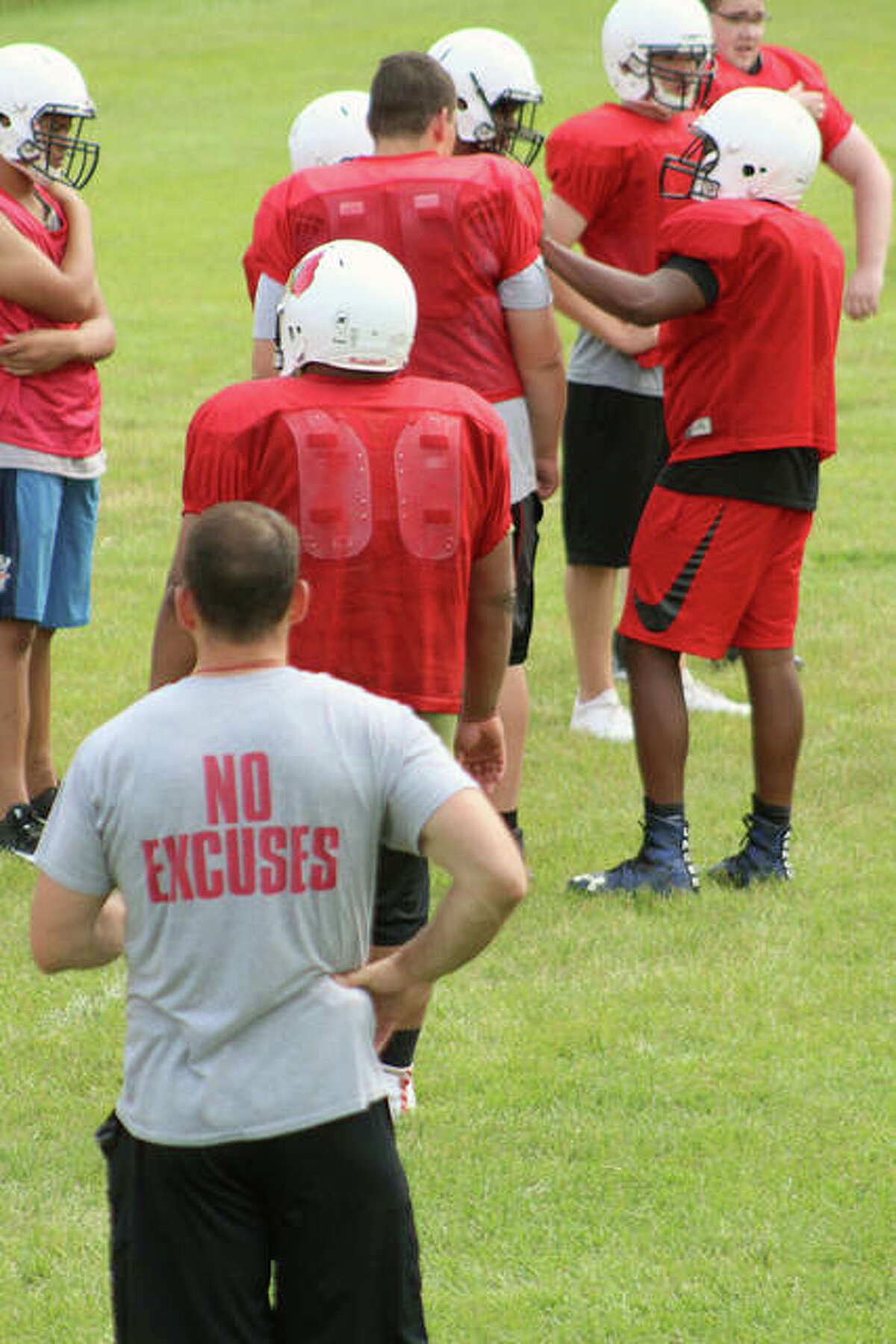 Alton High head coach Eric Dickerson, foreground, watches the line practice while his shirt sports a subliminal message during a summer contact session Tuesday at AHS.