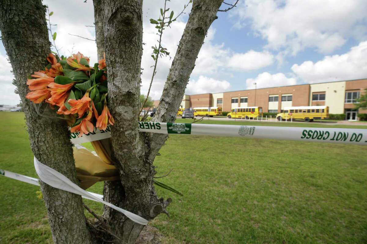 Memorial flowers sit among crime scene tape as buses transporating people to Santa Fe High School to retrive their belongings line up Saturday, May 19, 2018, one day after a mass shooting at the school left 10 people dead.