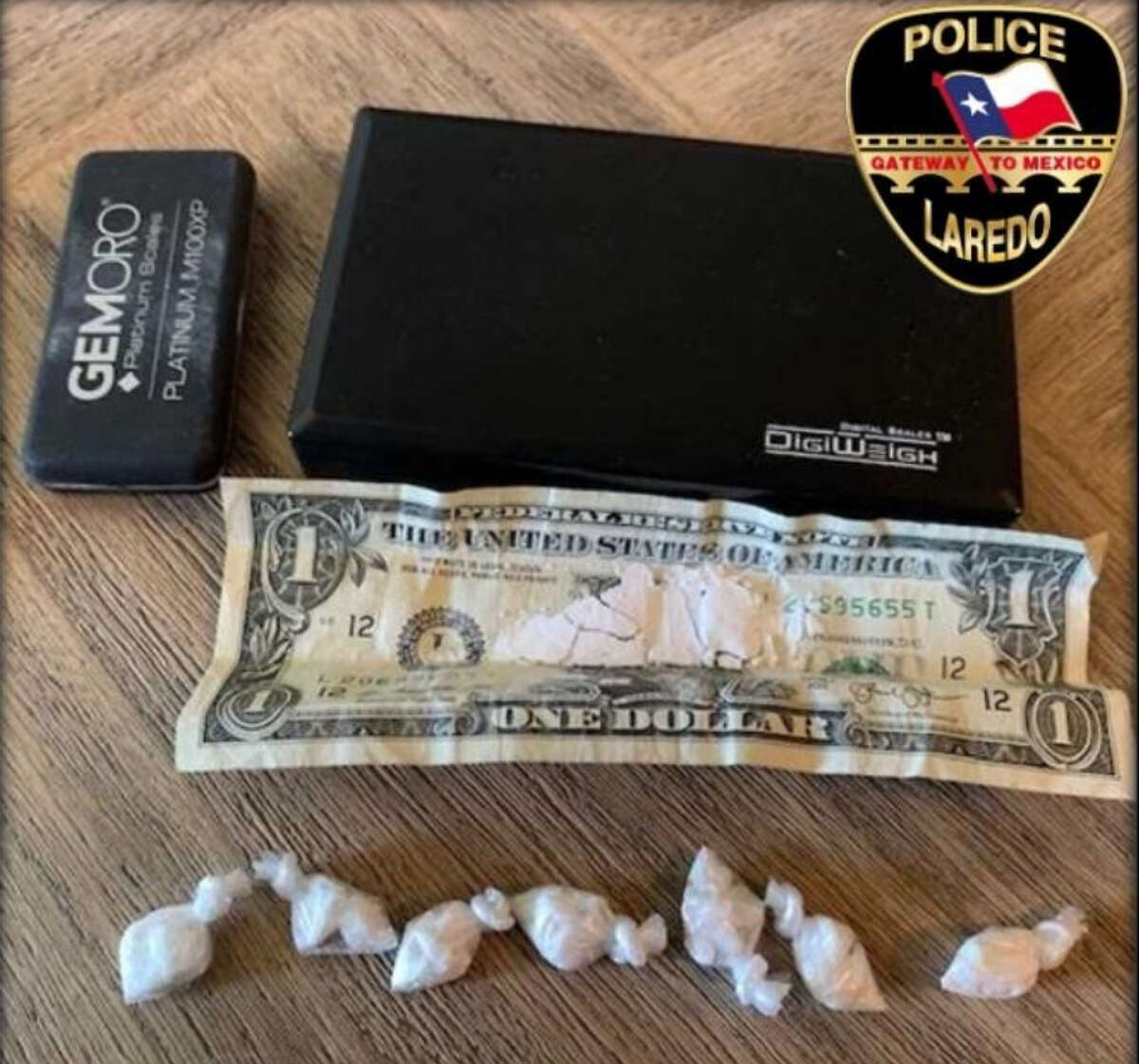 Shown is a dollar bill containing cocaine, seven plastic baggies containing cocaine and a digital scale.