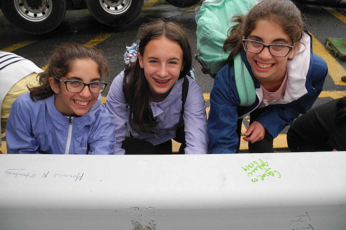 Alexis Shukovsky, 12, left, Courtney Allen, 11, and Madeline Shukovsky, 12, sign their names to a beam that will become part of the renovated Riverbrook Regional YMCA in Wilton, Conn., on June 13, 2019. Alexis and Madeline both swim for the Wilton Wahoos. —Jeannette Ross/Hearst Connecticut Media