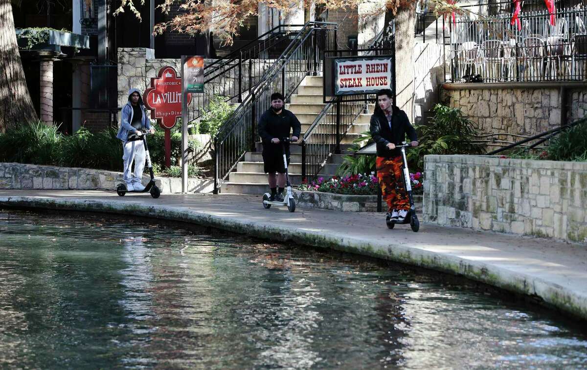 Three scooter riders are seen using the vehicles along the River Walk, which is prohibited by city ordinance, last December near La Villita. Starting Monday, the city will ban riding scooters on all sidewalks and assign three police officers to issue warnings to violators during a ‘grace period’ in July. (Kin Man Hui/San Antonio Express-News)