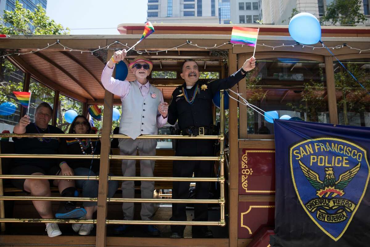 A couple waves holding flags from the San Francisco Police Department trolley taking part in the 2019 San Francisco Pride Parade on Market Street in San Francisco on June 30, 2019.