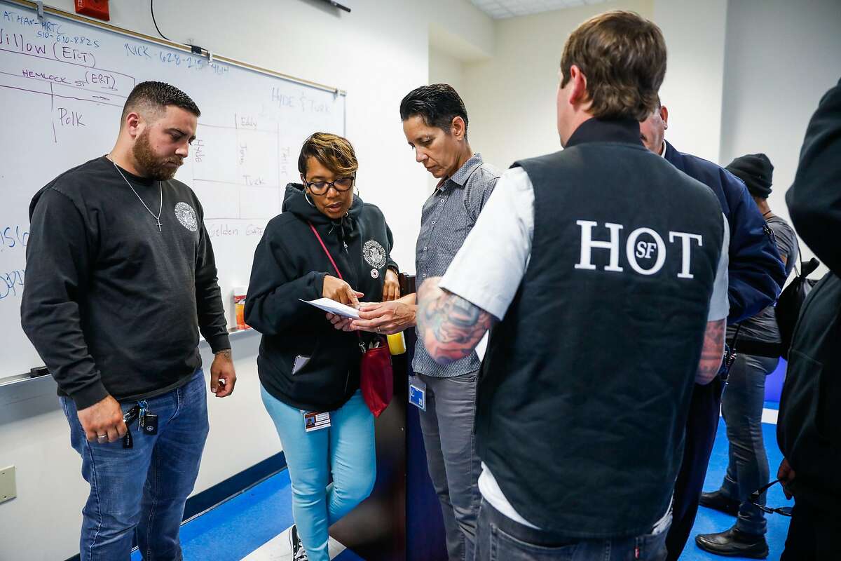 Carolyn Akbar (center, left) looks at paperwork with Brenda Meskan (center,right) during a Homeless Outreach Team meeting ahead of going out on the streets in the Tenderloin in San Francisco, California, on Wednesday, June 26, 2019.