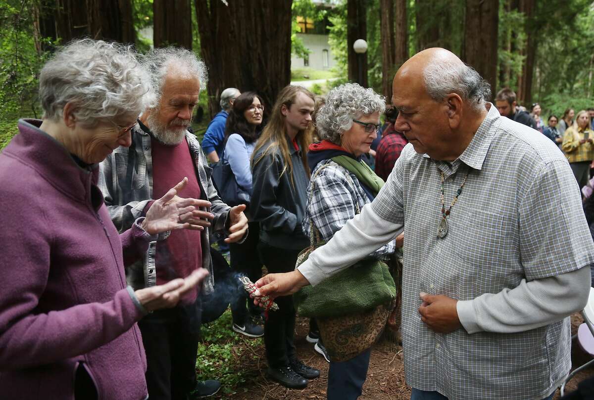 Valentin Lopez, Chair of the Amah Mutsun Tribal Band, right, blesses attendees with burning sage as members of the UC Santa Cruz administration and interested community members witness the removal of the El Camino Real bell marker on Friday, 6/21, 2019 at UC Santa Cruz in Santa Cruz, California. The bell marker, which memorializes the California Missions and an imagined route of travel that once connected them, is viewed by the Amah Mutsun and many other California indigenous people as a racist symbol that glorifies the domination and dehumanization of their ancestors. It is being removed at the request of the Amah Mutsun, with support from UCSC faculty members, students, and administrators.
