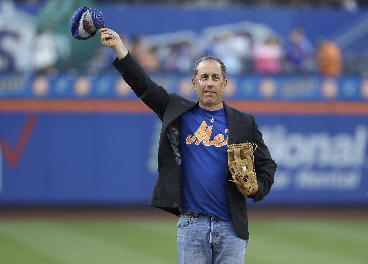 Comedian Jerry Seinfeld gestures to fans before throwing out a ceremonial first pitch before a baseball game between the New York Mets and the Philadelphia Phillies on Friday, July 5, 2019, in New York. (AP Photo/Frank Franklin II)