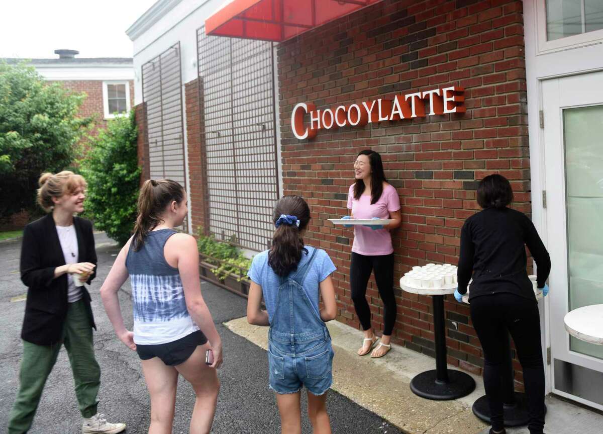 Jing Wu hands out free chocolate and cakes samples outside the new Chocoylatte Gourmet in the Cos Cob section of Greenwich, Conn. Monday, July 8, 2019. The official opening and ribbon-cutting was delayed due to an electrical issue, but folks still stopped by to receive samples and chat with employees.
