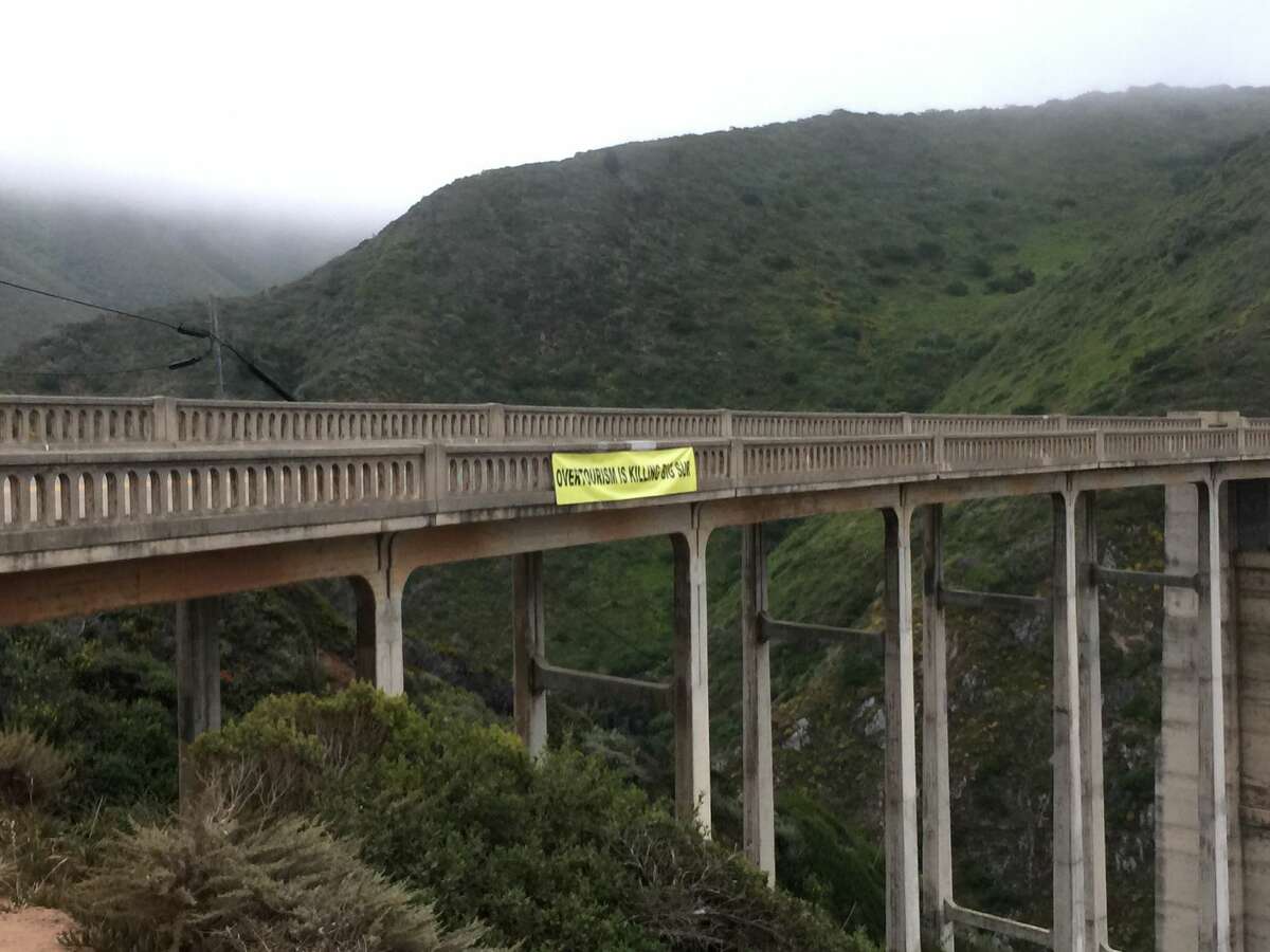 A banner reading "OVERTOURISM IS KILLING BIG SUR" hangs from Bixby Bridge in July 2019.
