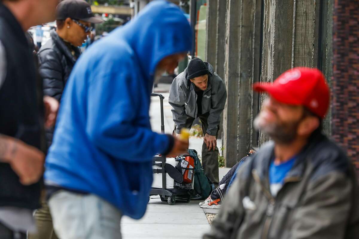 Department of Public Housing outreach worker Nick Lindley (center) chats with a homeless woman (not visible) in the Tenderloin in San Francisco, California, on Wednesday, June 26, 2019.