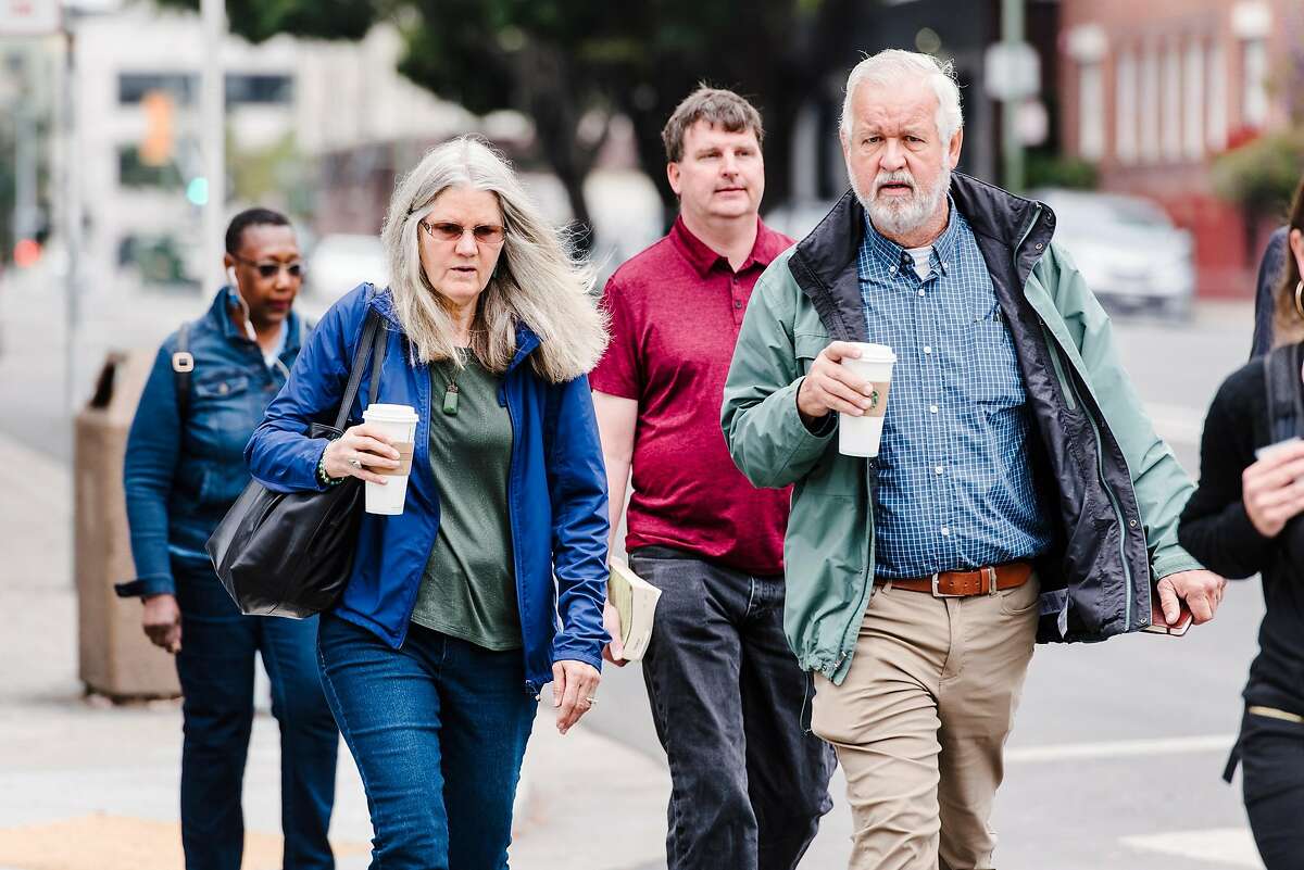 Susan Slocum, left, and husband Keith Slocum, mother and stepfather of Ghost Ship fire victim Donna Kellogg, walk towards the Alameda County Superior Court in Oakland, Calif., on July 9th, 2019, as main defendant Derick Almena is scheduled to take the stand for a second day.