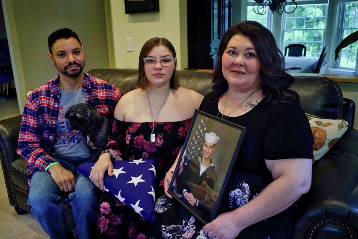 Michael and Jolee Hicks pose with their daughter Sienna, center, at their Capital Region home on Tuesday, June 18, 2019. Jolee Hicks is holding a photo of their son, Macoy, who killed himself while in a military brig. Sienna holds the flag from Macoy's funeral. (Paul Buckowski/Times Union)