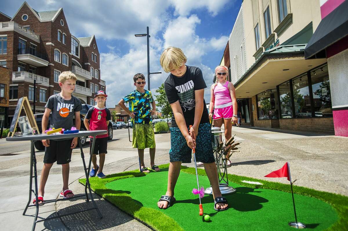 Grady Arnold, 7, lines up a putt while (from left) Evan Baczewski, 8, Keegan Arnold, 6, Erick Baczewski, 11, and Elee Arnold, 9, watch as the group plays mini golf on Wednesday, July 10, 2019 in downtown Midland. Mini Golf on Main, hosted by the Midland Downtown Business Association, will continue through this Saturday, July 13. (Katy Kildee/kkildee@mdn.net)