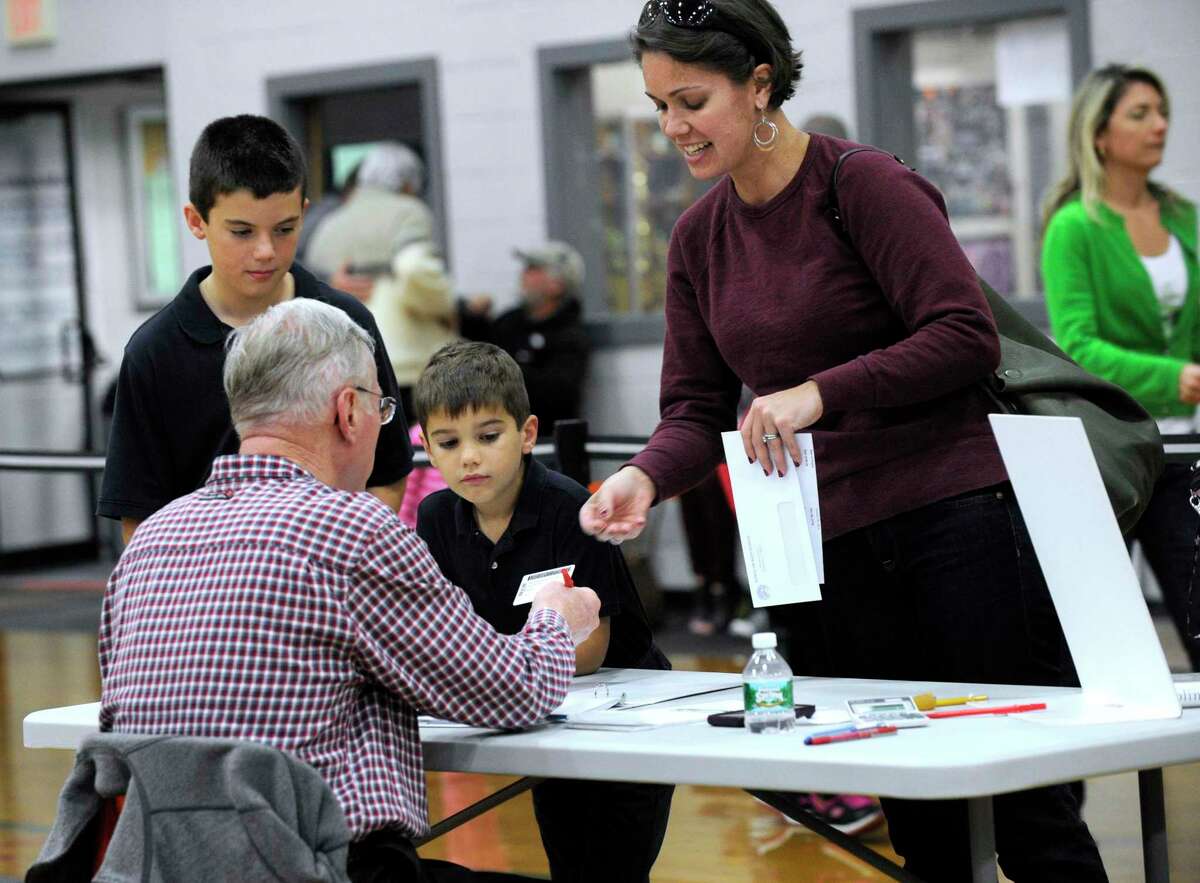 Joy Strand, with sons Joel, 9, and Jackson, 6, check in with official checker Doug Kleinmann at the Yanity Gym polling place Tuesday afternoon. The Yanity Gym, the district 3 polling place in Ridgefield, Conn. had a steady stream of voters Election Day, Nov. 4, 2014.