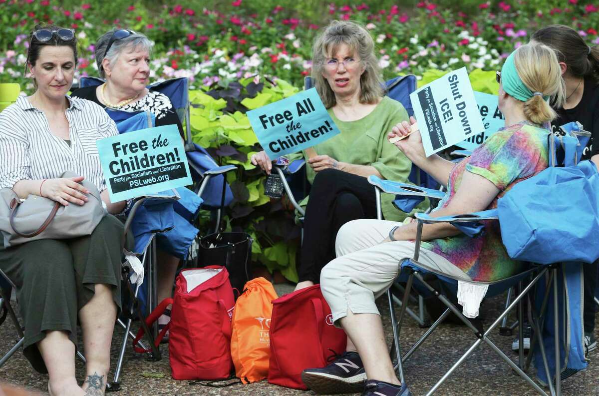 Signs are used as fans to beat the stifling late afternoon heat during the Lights for Liberty event at Travis Park on July 12, 2019.