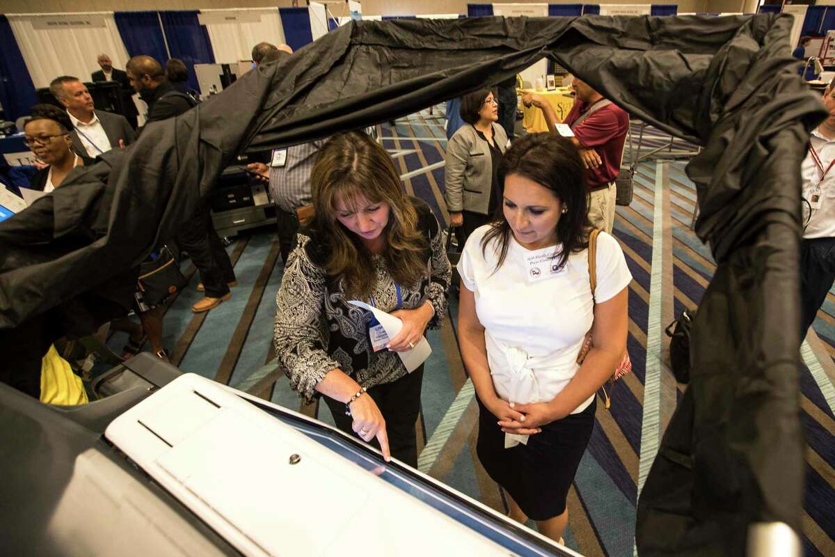 Christine Valeriano, left, demonstrates a voting machine during annual International Association of Government Officials (iGo) Conference Trade Show on Tuesday, July 16, 2019, in Houston. Trautman's office is looking to update voting technology in the near future.