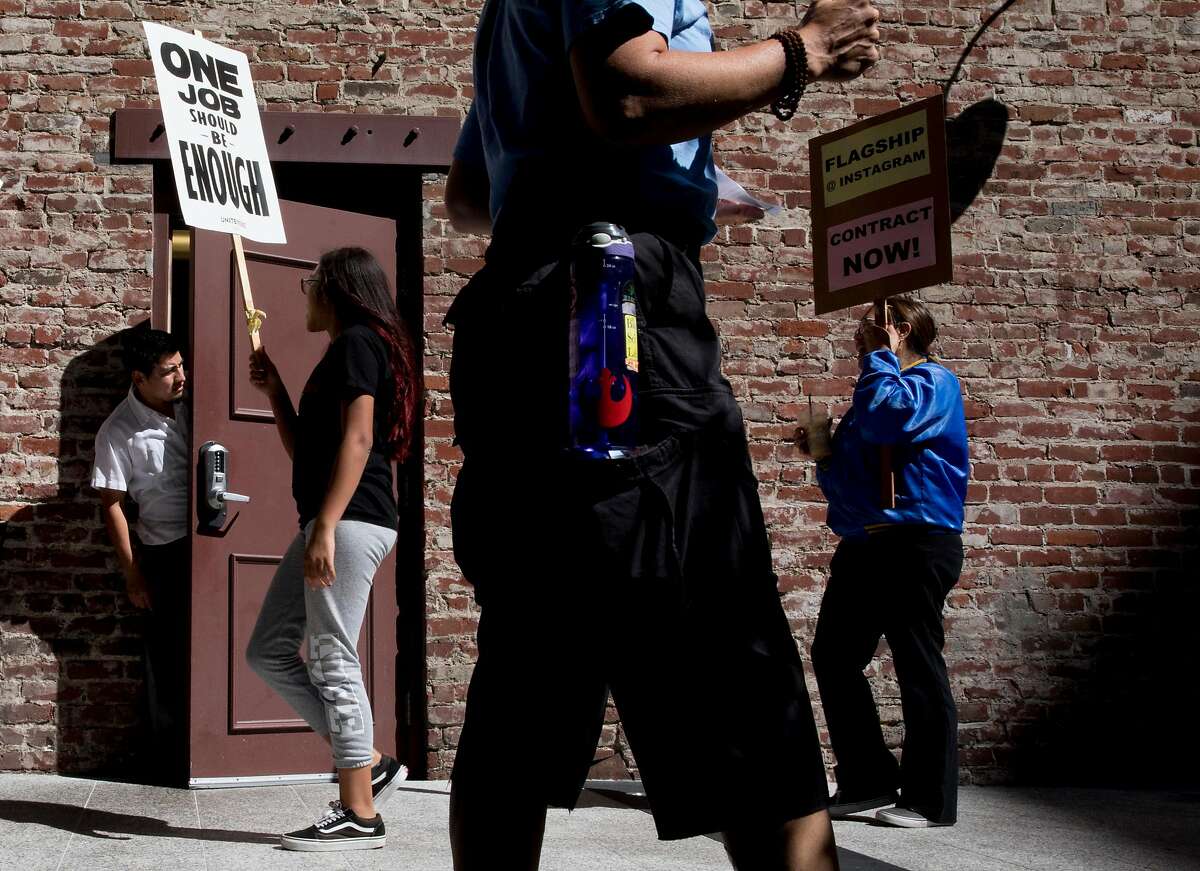 A restaurant worker pokes his head out of a nearby door to watch as Union Local 2 members, Flagship cafeteria contract workers and supporters march with signs during a protest held outside of the Facebook offices in San Francisco, Calif. Tuesday, July 16, 2019.