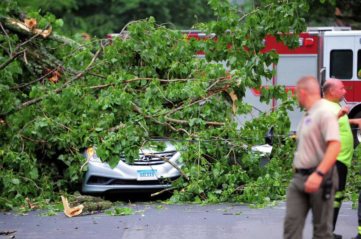 A car, with an occupant who was rescued from it, is still covered by a tree which fell on it along Park Ave Bridgeport, Conn., on Wednesday July 17, 2019. Due to live wires that fell, Bridgeport and Fairfield firefighters had to wait as long as an hour before they could remove the victim.