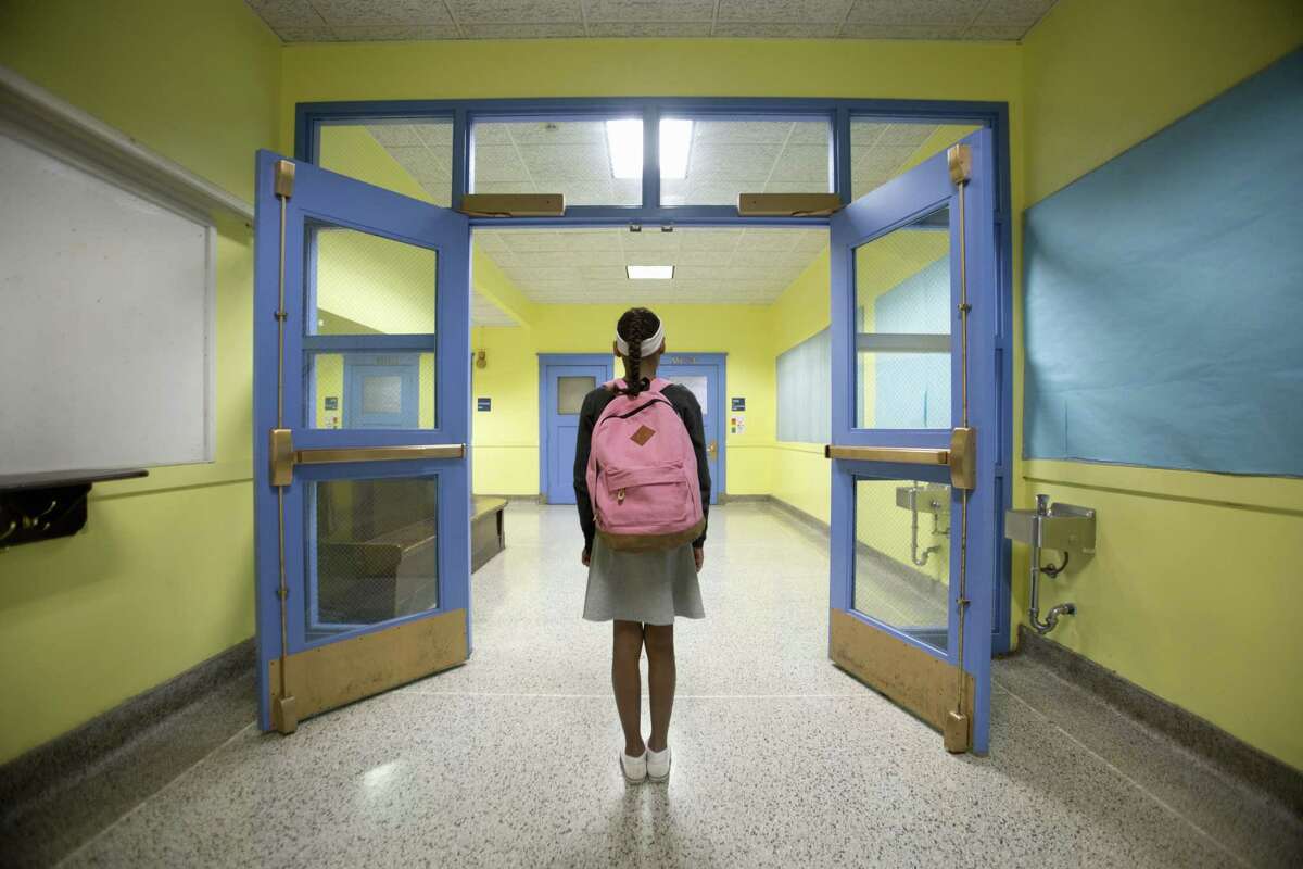 Rear view of eleven-year-old girl looking down school corridor.