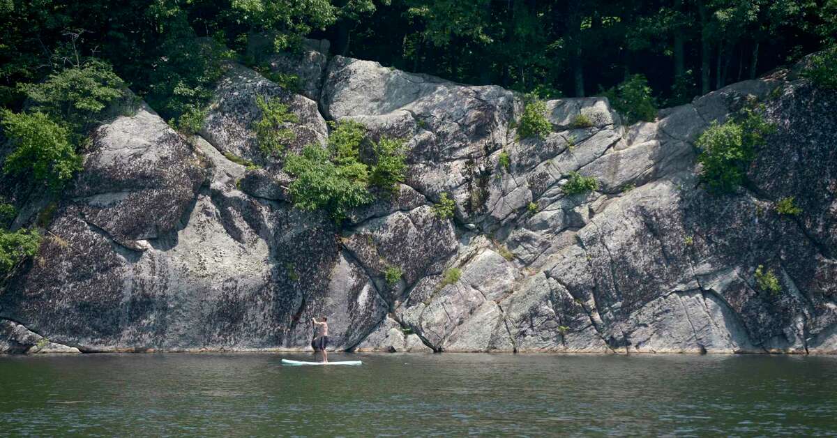 A paddle boarder glides by the cliffs on Mamanasco Lake. that are located in Richardson Park. Monday, July 22, 2019, in Ridgefield, Conn.