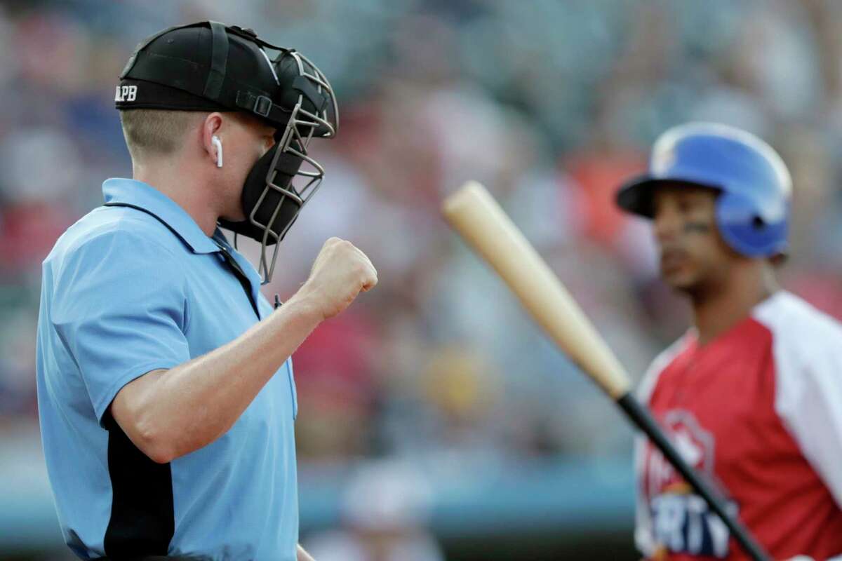 Home plate umpire Brian deBrauwere, left, calls a strike given to him by a radar system over an earpiece as Liberty Division's Tyler Ladendorf, right, of the High Point Rockers, strikes out to Freedom Division's Mitch Atkins, of the York Revolution, during the first inning of the Atlantic League All-Star minor league baseball game, Wednesday, July 10, 2019, in York, Pa. deBrauwere wore the earpiece connected to an iPhone in his ball bag which relayed ball and strike calls upon receiving it from a TrackMan computer system that uses Doppler radar. The independent Atlantic League became the first American professional baseball league to let the computer call balls and strikes during the all star game. (AP Photo/Julio Cortez)