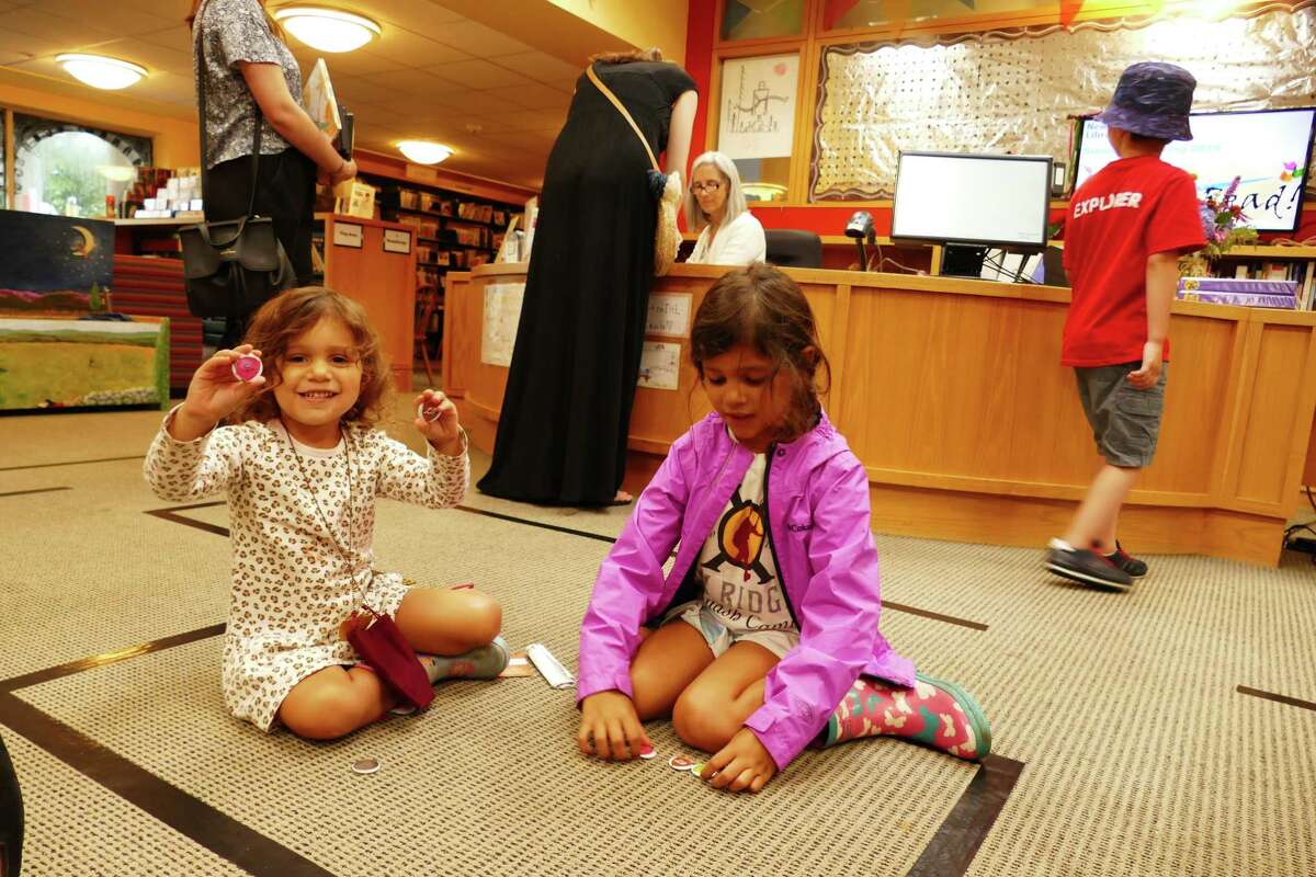 Serena Sordoni and her older sister Stella admire the button-like coins they earned as part of the Joust Read program at the New Canaan Library. They sat on the floor of the children's room on July 19.