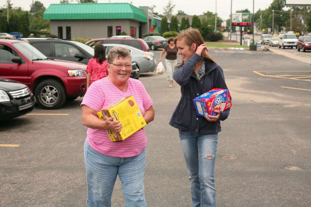 FOOD DONATION: Angels of Action volunteer Amanda Falk (right) helps carry boxes of food donated by Carol Kelley (left) during a food drive on Thursday at Family Video in Big Rapids. The event kicked off the nonprofit’s summer food drive schedule. (Pioneer photos/Jonathan Eppley)
