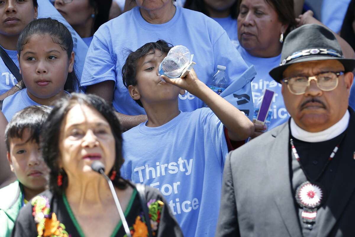 FILE - in this June 10, 2019 file photo a young man sips some water as civil rights activist Dolores Huerta, left, speaks in support of a clean water measure before the legislature, during a rally in Sacramento, Calif. Gov. Gavin Newsom signed a law Wednesday, July 24, 2019, that will redirect up to $130 million of state money meant to clean up the air to instead clean up the drinking water for more than 1 million Californians who don't have clean drinking water. (AP Photo/Rich Pedroncelli, File)