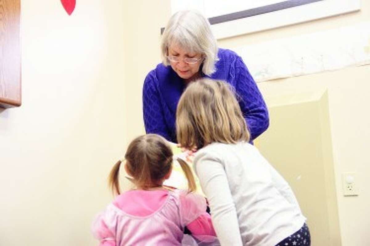 YOUNG LISTENERS: Two children, not yet old enough for school, enjoy hearing Candy Derevage – known as Mrs. D – read during Story Hour at Reed City Library. Derevage has read to many children in the Reed City community during her 20 years at Reed City Library. (Pioneer photo/Sarah Neubecker)