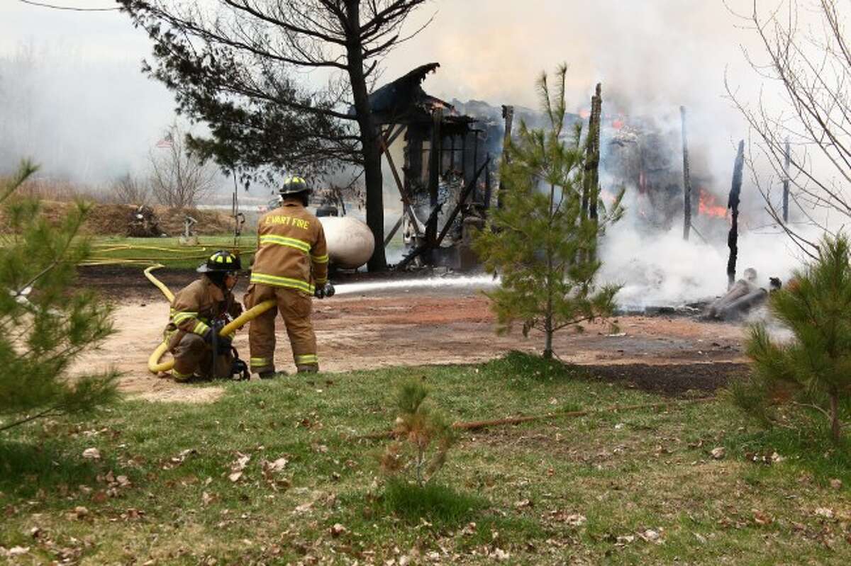 BURN: Evart Fire Department firefighters hose down the remains of the smoking garage to make sure the flames are fully extinguished.