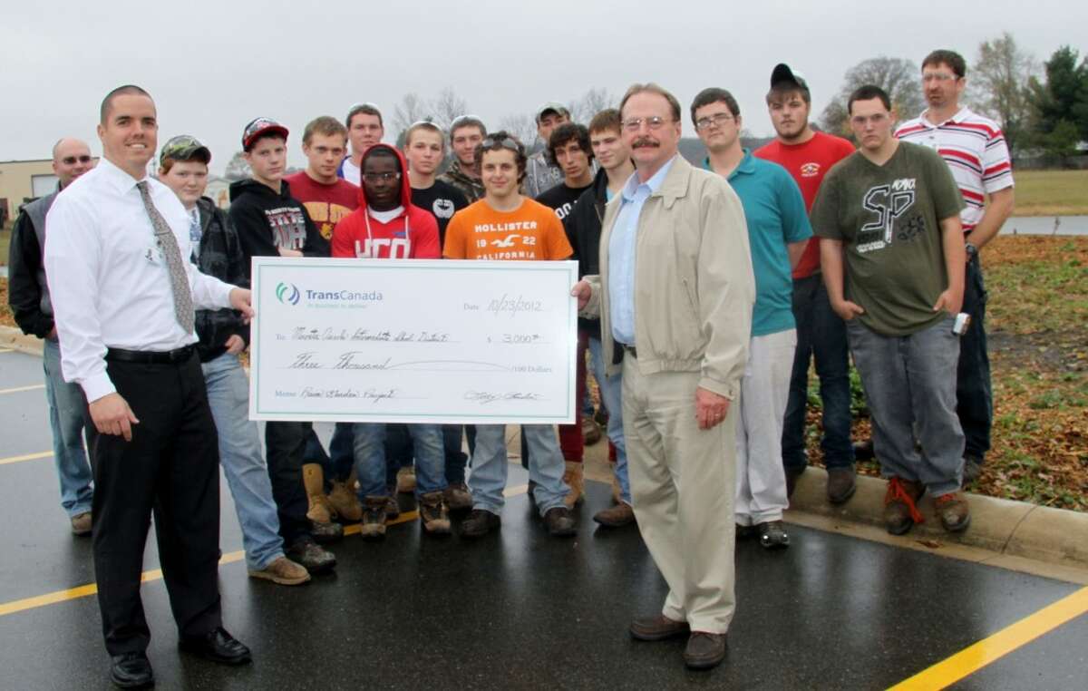 LEARNING OPPORTUNITY: (On left) MOCC Principal Steve Locke accepts a check for $3,000 from Larry London, community investment representative for TransCanada Corp., which donated the funds for a bridge over the MOCC’s rain garden. Also pictured are students in the Integrated Construction Technology program, who will design and build the bridge. (Pioneer photo/Lauren Fitch)