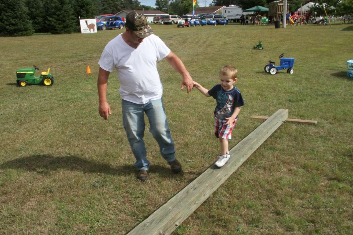 A HELPING HAND: Rob Livermore, of Munising, holds his nephew Braden's hand as he walks across a pole during Double D Farms' Farm Days in Weidman. (Pioneer photos/Eric Dresden)