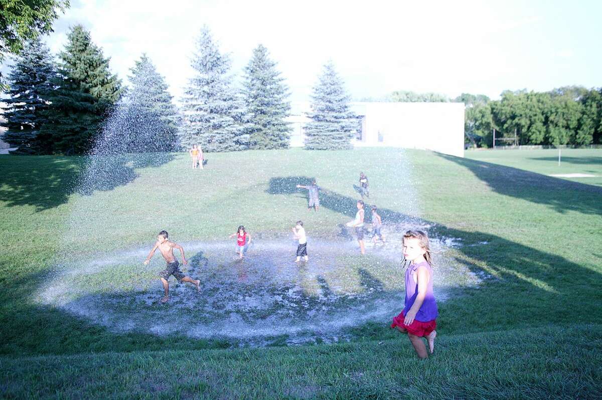 KEEPIN’ COOL: Children play under a fire hose fountain on the Big Rapids Middle School lawn.