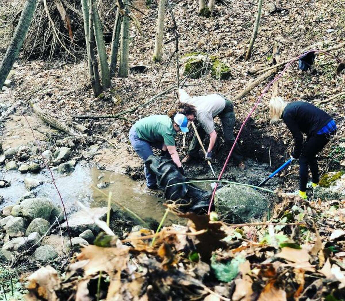 Volunteers work to remove a tractor tire from a creek along the Fred Meijer White Pine Trail on Sunday.