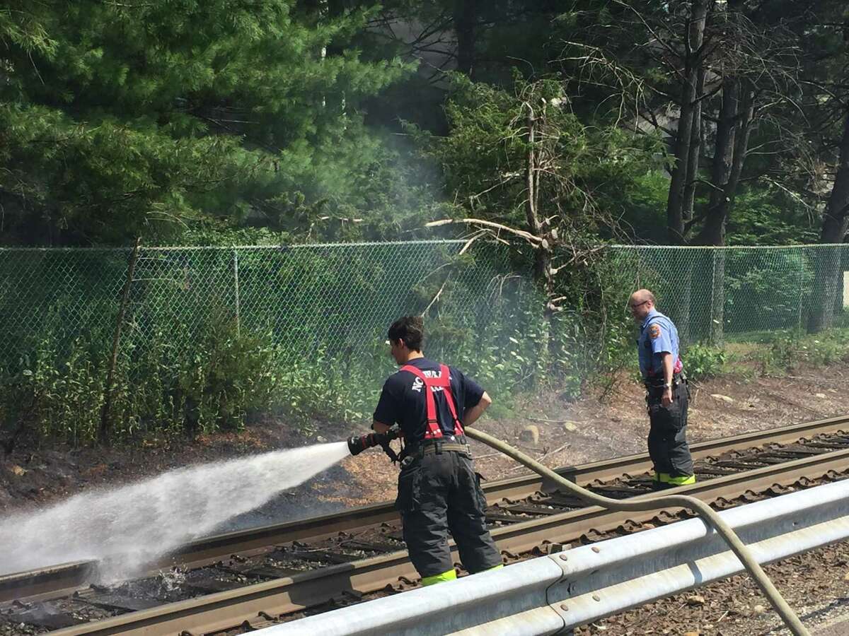 Norwalk firefighters from Engine 1 douse flames along the Danbury Line of Metro-North on Friday afternoon. The brush fire was across from 87 Glover Ave., just north of the station platform.