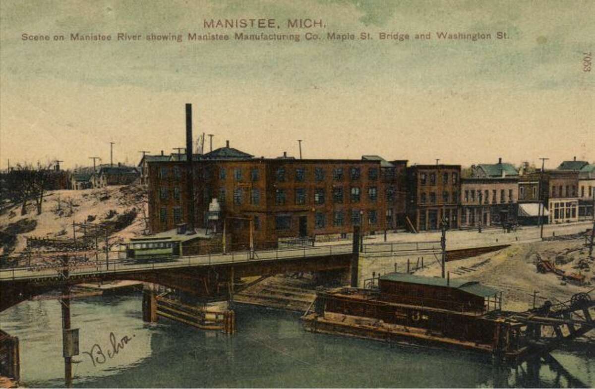 This late 1890s picture shows the Manistee River with the Manistee Manufacturing Company and the Maple Street Bridge with a trolley going across it.