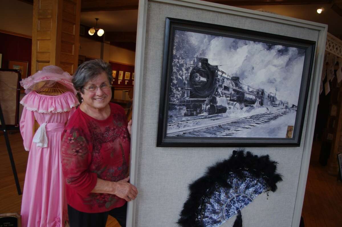 Jan Kenny’s favorite painting features a locomotive, and was done in honor of her father, a fireman for the Pennsylvania Railroad. Behind Kenny is the Victorian dress she wore as Victoria Port City in the early days of Manistee’s efforts to discover its uniqueness and Victorian heritage. Kenny’s lifetime art exhibit is on display at the Ramsdell Theatre through Thursday. (Dave Yarnell/News Advocate)