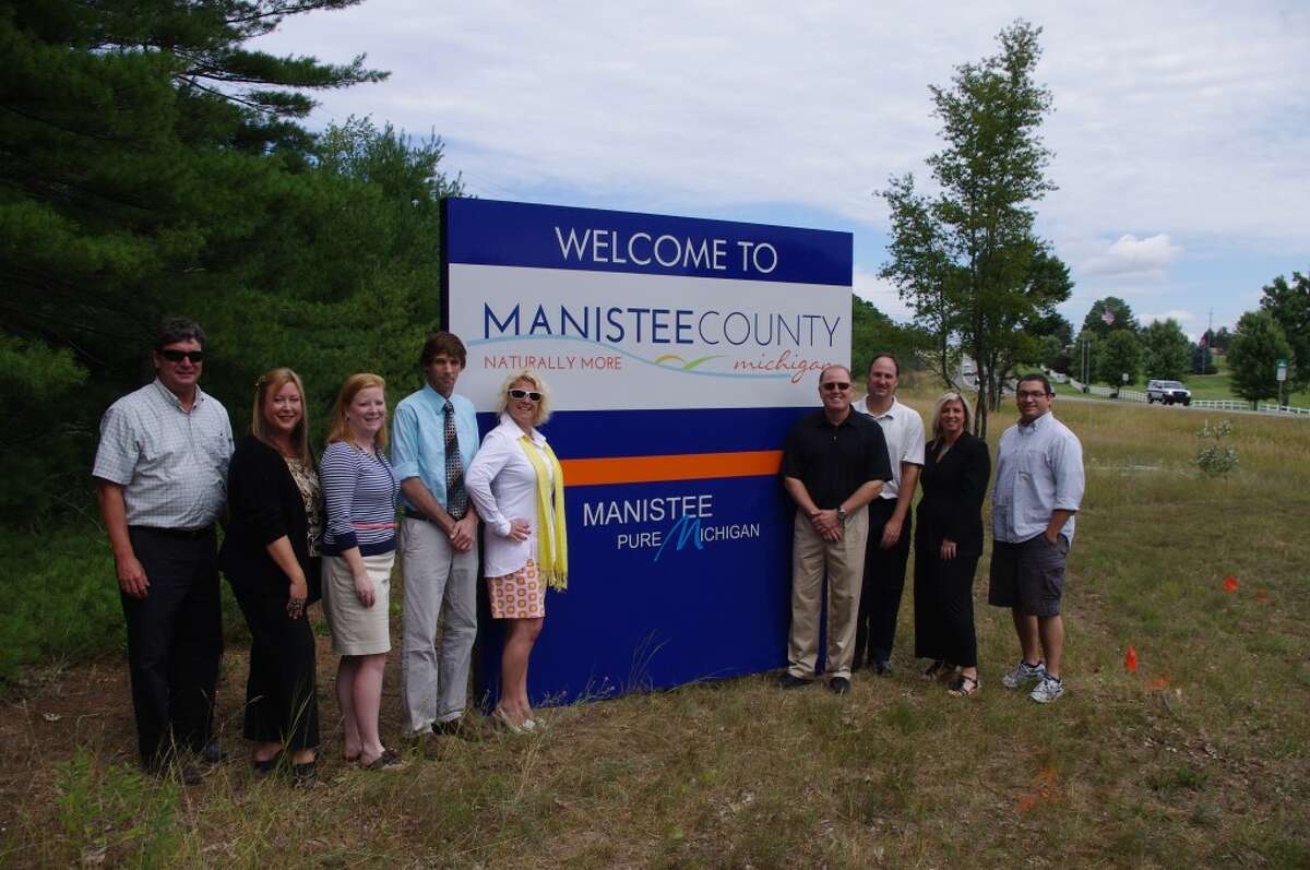 Officials of the Manistee County Visitors Bureau met at the U.S. 31 south county line on Friday to see the new welcome sign placed there. (From left to right) are Tom Amor and Deborah Nale of Amor Sign Studios; Taryn Anderson of West Shore Bank; Chuck Smith of Manistee Super 8; Kathryn Kenny, executive director of the Manistee County Visitors Bureau; Doug Bell, Manistee National Golf & Resort; Todd Newenhouse, Manistee Days Inn; Suzanne Riley, Century 21 Boardwalk; and Travis Alden, executive director of the Manistee Main Street Downtown Development Authority. (Dave Yarnell/News Advocate)