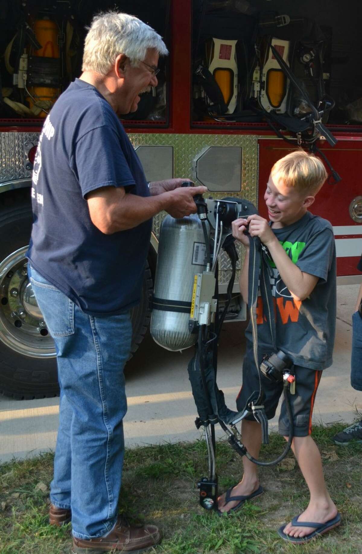 Norman Township Fire Chief John Gramza (LEFT) laughs as Tyler Duncan (RIGHT) attempts to lift a compressed air canister, a part of a firefighter's equipment that weighs between 25 and 50 pounds. (Meg LeDuc/News Advocate)