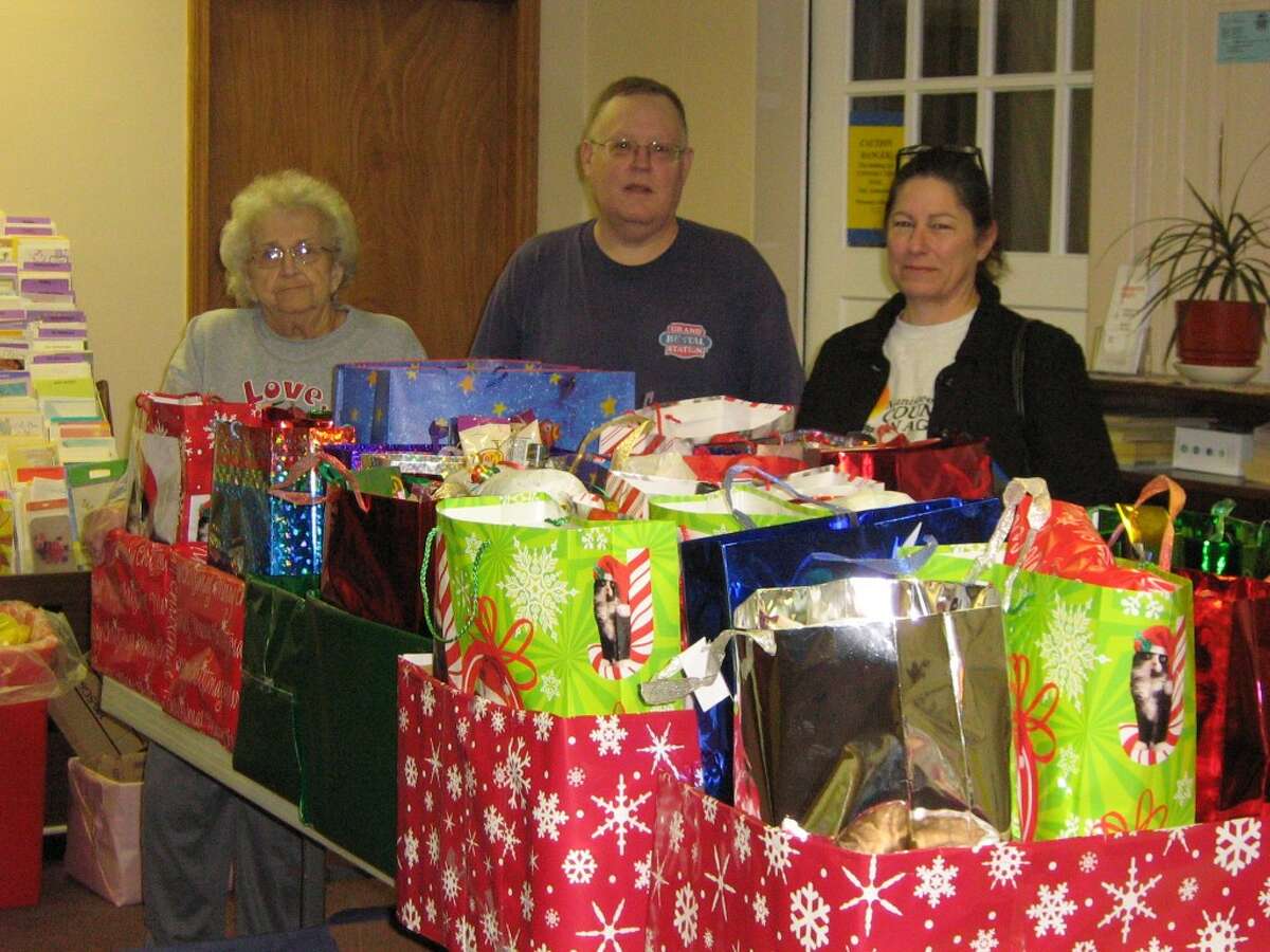 Manistee County Council on Aging employees, from left, Patricia Bush, Ken Schwalm and Debbie Tarnowski appear with Christmas gifts that they collected, wrapped and delivered to adult foster care home residents. (Courtesy Photo)
