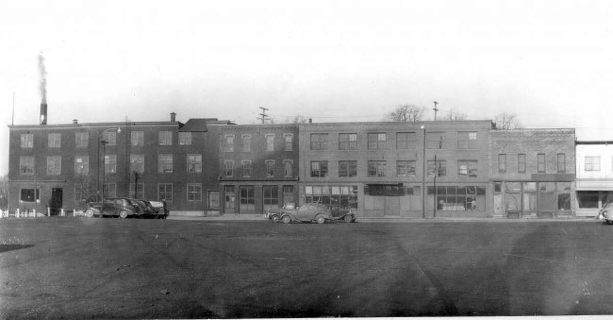 Shown is a group of buildings on Washington Street on the north side of the Maple Street bridge. The Manistee Manufacturing company is the building on the on the lest of this picture from the late 1940s.