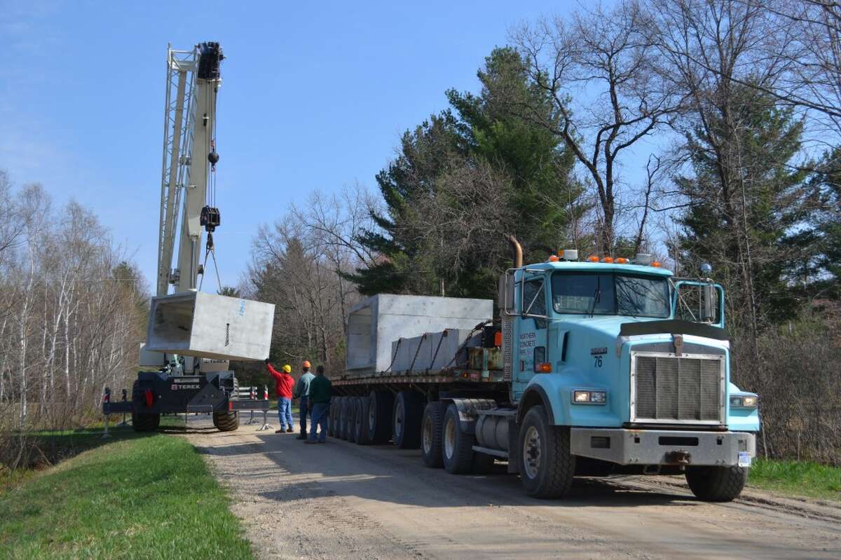 Manistee County Road Commission employees, assisted by an employee of Northern Concrete Pipe, unload a section of concrete culvert from a trailer at Kettle Hole Road on Thursday. Work is underway to relieve flooding by replacing the old culvert with a new, significantly larger one. (Meg LeDuc/News Advocate)